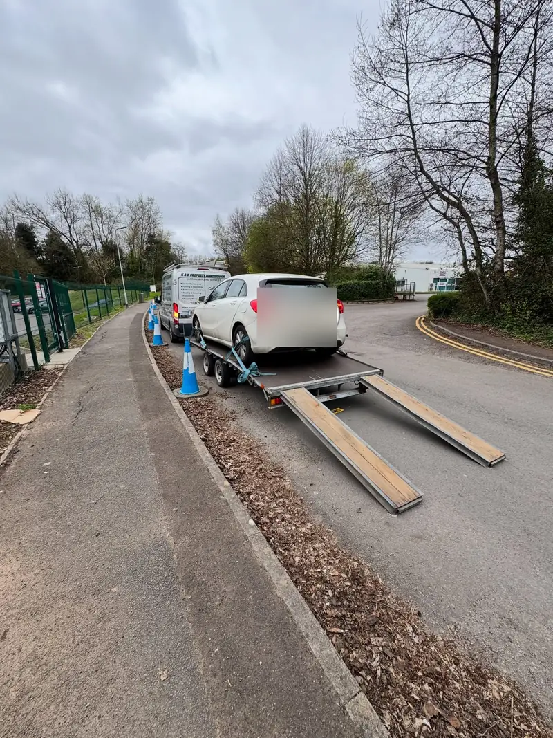 White car being loaded onto a trailer by ramps at the roadside with cones out